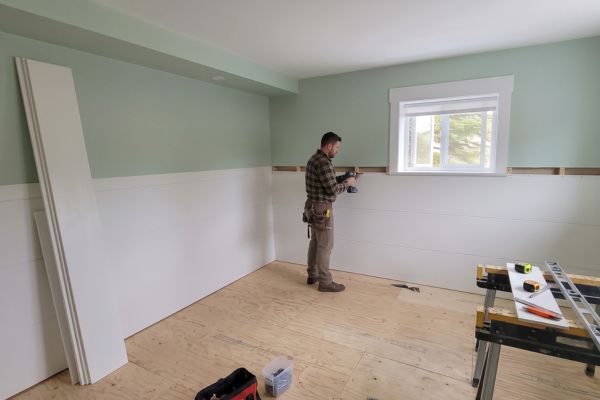 Installer fastening a white Trusscore panel to the studs, with spare panels leaning against the wall